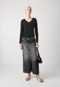 Svart v-utringet genser kombinert med en lang, mørkegrå denimskjørt med en frontsliss. Modellen holder en liten svart veske og har på seg hæl sandaler.