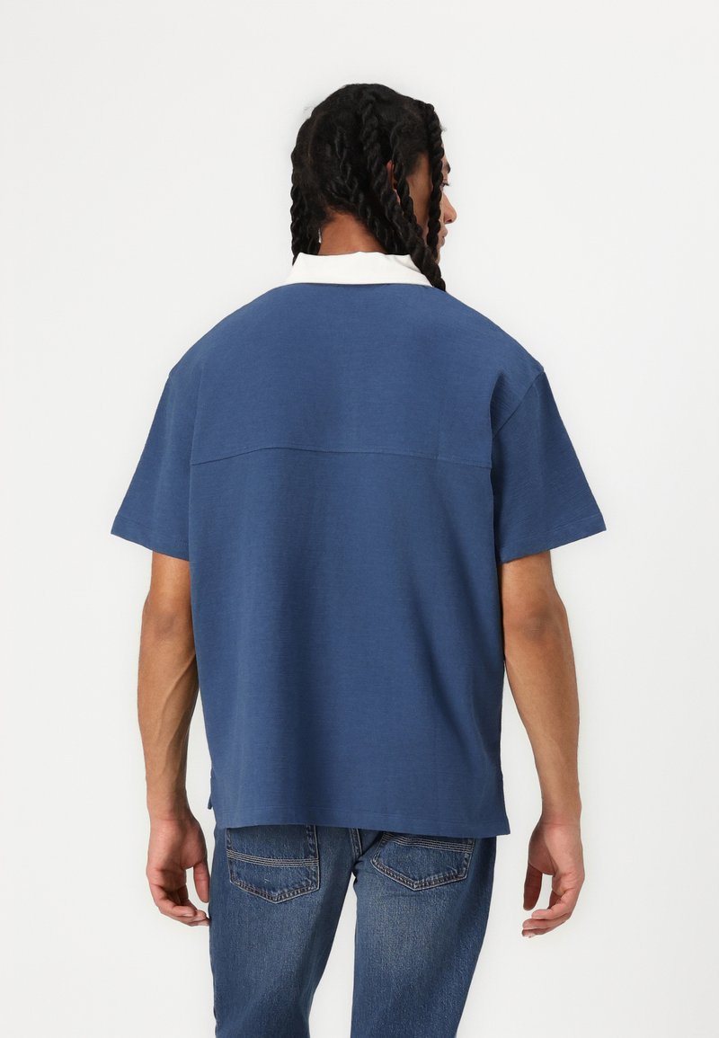 Polo shirt à manches courtes bleu marine avec un col blanc, présentant une coupe décontractée, une texture douce et un détail de couture subtil à l'arrière.