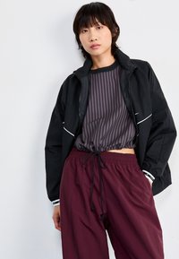 Svart zip-up jacka, lila randig skjorta med dragsko och burgundy byxor med elastisk midja. Funktioner inkluderar vita detaljer och en avslappnad passform.