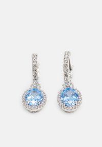 Strieborné kruhové náušnice s veľkým okrúhlym modrým drahokamom obklopeným menšími čírymi kryštálmi na ozdobe a kruhu.