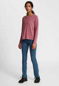 Langarmig, rozenkleurig shirt met een ronde hals, gecombineerd met blauwe sportbroeken en zwarte sneakers. Eenvoudig ontwerp met een klein logo.