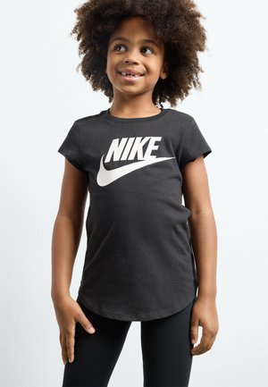 T-shirt en coton noir avec un ourlet arrondi et des manches courtes, arborant un grand logo Nike blanc sur la poitrine. Porté avec des leggings noirs.