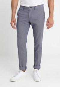 Pantaloni leggeri a scacchi grigi, con risvolti, tasche frontali e chiusura con bottone. Indossati con sneakers bianche.