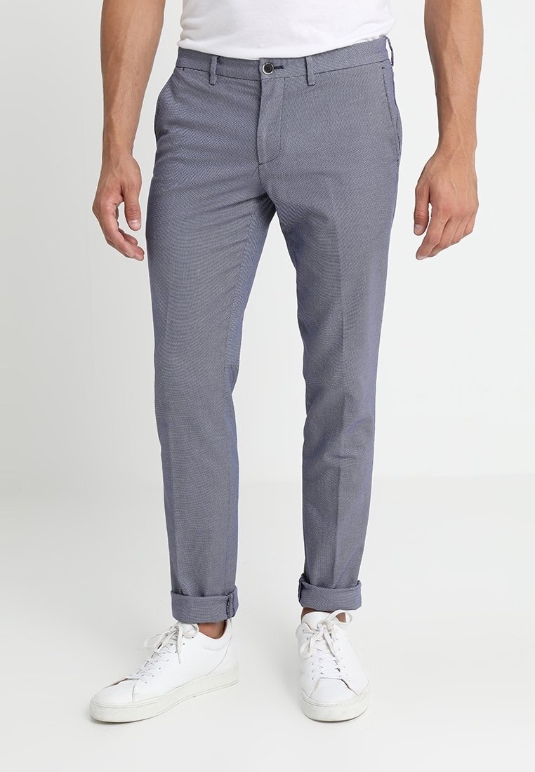 Pantaloni leggeri a scacchi grigi, con risvolti, tasche frontali e chiusura con bottone. Indossati con sneakers bianche.