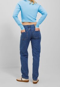 Hochgeschnittene blaue Jeans mit geradem Schnitt, ausgestattet mit zwei Gesäßtaschen und einem lockeren Sitz, kombiniert mit einem hellblauen Langarmoberteil.