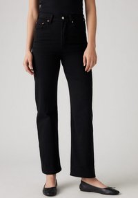 Zwarte, hooggetailleerde jeans met rechte pijpen, vijfzakkenontwerp, koperen accenten en een gladde denimbinding. Gecombineerd met zwarte ballerina's.