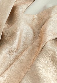 Gros plan sur un tissu doré clair et brillant avec une texture douce et des plis et rides visibles.