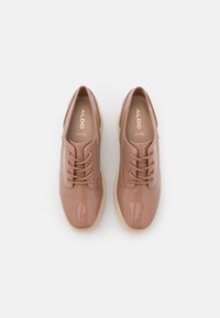 Chaussures Oxford en cuir verni beige avec un bout arrondi, un laçage à l'avant et une semelle de couleur claire. Logo imprimé sur la semelle intérieure.
