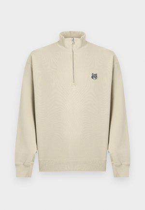 Bēšs ceturtdaļas rāvējslēdzēja džemperis ar garām piedurknēm un ribotām aprocēm, kreisajā krūtīs neliels vilka galvas logotips.