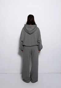 Szary skrócony hoodie z kapturem i długimi rękawami, zestawiony z szerokimi spodniami w tym samym odcieniu. Posiada różowe akcenty na rękawach. Miękka tekstura materiału.