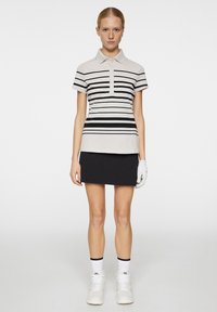 Koszula polo z kołnierzykiem w jasnym beżu z czarnymi poziomymi paskami, zestawiona z czarną spódnicą. Ubranie zawiera białą rękawiczkę i sneakersy.