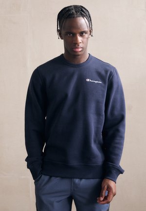 Sudadera azul marino hecha de un tejido suave, con un cuello redondo y el logo de "Champion" bordado en blanco en el lado izquierdo del pecho.