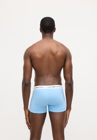 Lyseblå boxershorts lavet af glat stof med en hvid elastisk linning med røde og blå logodetaljer.