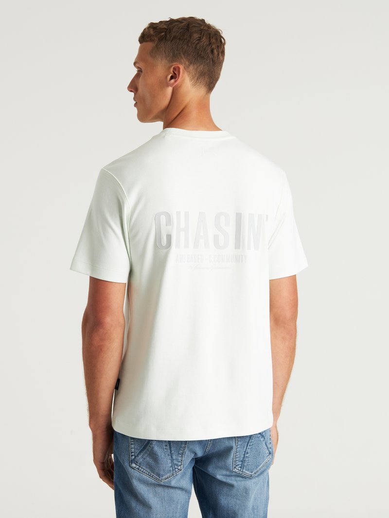 Tricou scurt cu mânecă scurtă, de culoare verde deschis, cu o textură moale. Prezintă un logo mare, embosat "CHASIN'" pe spate. Este asociat cu blugi albaștri.