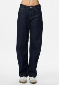 Klasiski tumši zili platā kāju džinsi ar piecām kabatām un smalku dzelteno šuvi. Pabeigti ar metalizētu pogu aizdari.