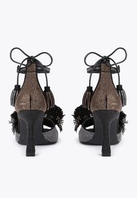 Czarne i metaliczne szpilki z wyciętym wzorem, ozdobione koralikami, frędzlami oraz teksturowaną powierzchnią; regulowane sznurki z tyłu.