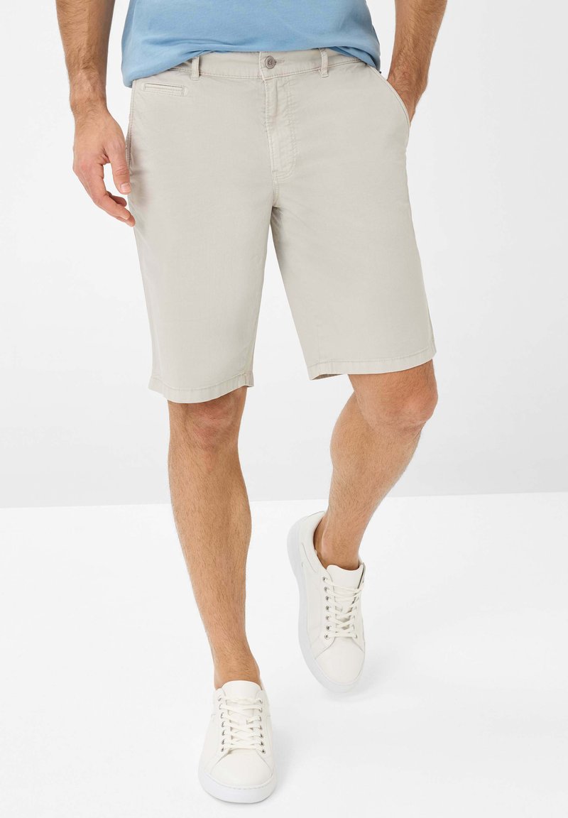 Beige shorts met een rechte snit, voorzien van een knoopsluiting aan de voorkant en zijzakken. Gecombineerd met witte sneakers voor een casual look.