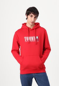 Felpa con cappuccio rosso e tasca anteriore, caratterizzata da un logo grafico bianco e dettagli in contrasto. Realizzata in tessuto morbido con una vestibilità casual.