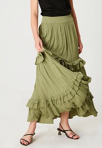 Jupe maxi plissée vert clair avec un ourlet volants, dotée d'une taille élastique et d'une silhouette fluide, complétée par des sandales noires à lanières.