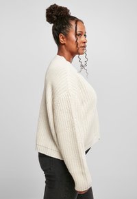 Ljus krämfärgad, tjock stickad tröja med en kort design, rund halsringning och ribbad nederkant; bärs med mörka jeans.