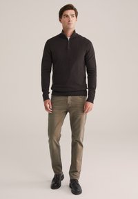 Schwarzer Reißverschluss-Pullover aus Strickstoff, kombiniert mit olivgrünen Jeans und schwarzen geschnürten Schuhen. Die Passform ist schlank mit gerippten Bündchen und Saum.