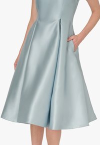 Jasnoniebieska sukienka z satyny z dopasowanym gorsetem, szeroką plisowaną spódnicą i bocznymi kieszeniami. Gładka faktura i elegancka sylwetka delikatnie się układają.