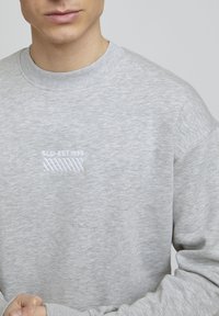 Sweatshirt gris avec une texture douce, col côtelé et logo brodé "SLD-EST.1999" en blanc sur la partie gauche de la poitrine.
