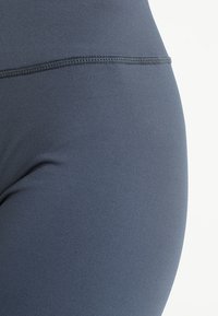 Detailní záběr na námořnickou modrou pružnou tkaninu s viditelným švem, těsně přiléhající k zakřivenému povrchu.