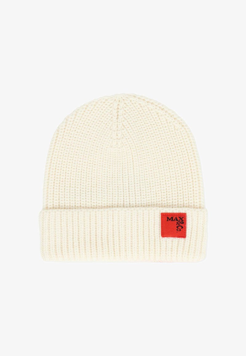 Crème gebreide beanie met een geribbelde textuur, met een omgeslagen zoom en een klein rood label met zwarte tekst aan de zijkant.