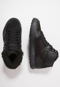 Svart høye sneakers med en teksturert skinnoverflate, med for av falsk pels, metalløye og gummisåle.