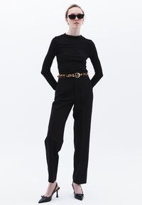 Svart långärmad topp, högmidjade svarta byxor med ett leopardmönstrat bälte, svarta slingback-klackar och mörka solglasögon. Minimalistisk stil.