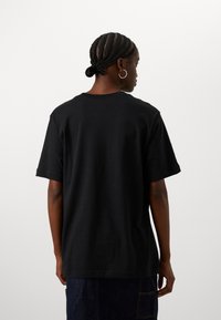 Camiseta de algodón negra de manga corta, con cuello redondo y un corte holgado; detalles de costura visibles en el dobladillo; combinada con una falda de mezclilla oscura.
