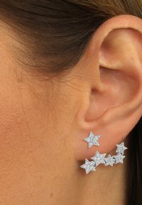 Boucles d'oreilles en forme d'étoile argentée avec cinq étoiles, certaines ornées de cristaux transparents, exhibant différentes tailles et positions le long de l'oreille.