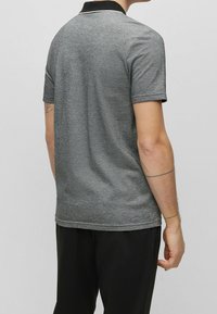 Grå kortärmad polo med svart krage och vit kant; slät textur, figurnära design och ribbad ärmkanter.