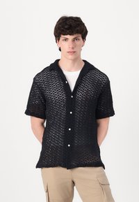 Camisa negra de manga corta con un patrón de punto texturizado y un cuello tipo polo, con botones blancos y un corte relajado.