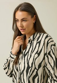 Camisa de botones color crema con llamativos rayas de cebra en negro, cuello y mangas largas con puños abotonados; confeccionada con un tejido texturizado.