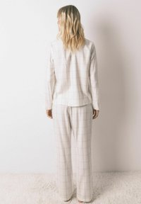 Hvid plaid loungewear sæt bestående af en langærmet top og løstsiddende bukser, lavet af blødt stof med en glat overflade.