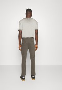 Camiseta cinza com gola redonda e mangas com punho, combinada com calças verdes-oliva com bolsos traseiros. Ténis pretos com detalhes brancos.