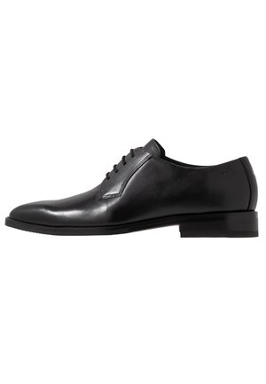 Zapato negro de cuero con cordones, acabado suave, punta redondeada y diseño minimalista. Presenta un tacón bajo y apilado con sutiles detalles de costura.