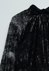 Sort blonde stof med blomster mønstre og lodrette sølvfarvede paljetter på en højhalset beklædning.