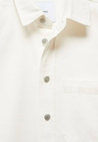 Camicia bianca con bottoni in stile button-up realizzata in tessuto testurizzato; presenta bottoni argentati, un colletto e una tasca sul petto.
