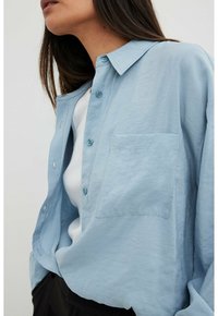 Light blue button-up shirt made of a soft, textured fabric. Features a collar, long sleeves, and a chest pocket.