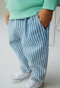 Hellblau-weiß gestreifte Hose mit weiter Passform und Seitentaschen, kombiniert mit weißen Sneakers und einem mintgrünen Sweatshirt.