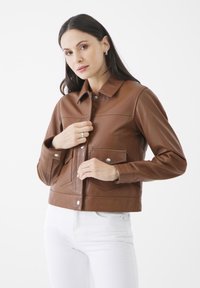 Brun läderjacka med kort passform, krage, tryckknappsstängning, två framfickor och sydda detaljer. Kombinerad med vita jeans.