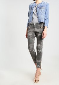 Veste en denim bleu clair, t-shirt gris, jean skinny à motifs camouflage dans des tons adoucis, et talons métalliques à brides.