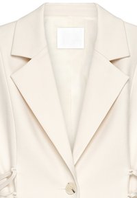 Blazer ajustado beige con solapa, cierre de un solo botón y lazos ajustables en los laterales. Tejido suave con una textura lisa. Etiqueta de NAKD visible.
