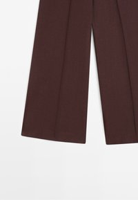 Pantaloni marroni a gamba larga con pieghe, mostrati dalla metà coscia fino all'orlo su sfondo bianco.