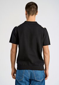 Svart kortärmad polo med texturerad stickning och ribbad nederkant. Har kontrasterande detaljer på axlarna och en klassisk kragsdesign.