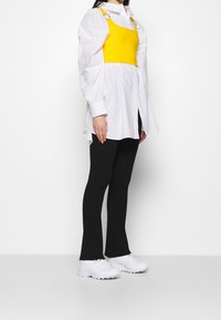 Keltainen ribatulla pinta crop-topi, joka on kerrostettu valkoisen nappipaidan päälle. Mustat leveät housut ja valkoiset lenkkarit täydentävät asua. Minimalistinen muotoilu.