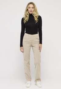 Black long-sleeve turtleneck paired with beige straight-leg pants. The outfit features a classic fit and a smooth texture. White sneakers complete the look.